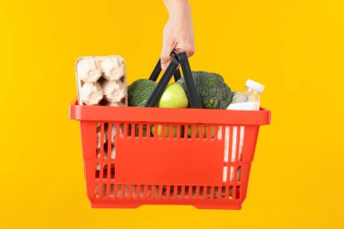 Sarı arka planda farklı ürünleri olan alışveriş sepeti tutan adam, yakın plan.