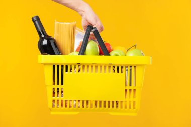 Sarı arka planda farklı ürünleri olan alışveriş sepeti tutan adam, yakın plan.