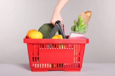 Gri arka planda ürünlerle dolu alışveriş sepeti olan kadın, yakın plan.