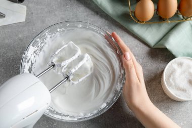 Gri desenli masada el çırpma kremi kullanan bir kadın.