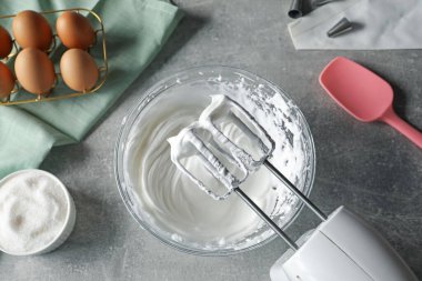 El karıştırıcı, bir kase krem şanti ve gri desenli masa üzerindeki malzemeler.