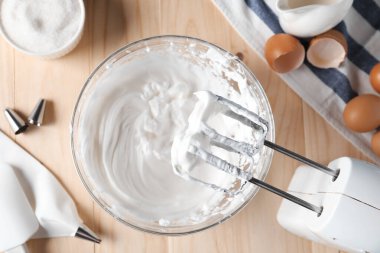 El çırpıcı, bir kase krem şanti ve ahşap masada malzemeler.