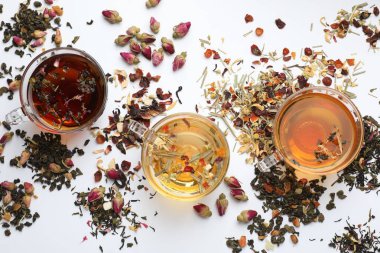 Beyaz arka planda farklı bitkisel çaylar ve kuru yapraklar.