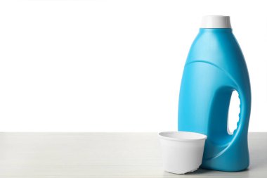 Beyaz arka planda bir şişe yumuşatıcı ve ahşap masa üzerinde kapak