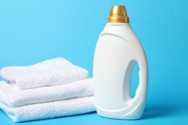 Bir şişe yumuşatıcı ve açık mavi arka planda havlular.