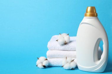 Bir şişe yumuşatıcı, pamuk çiçekleri ve açık mavi arka planda havlular, metin için alan