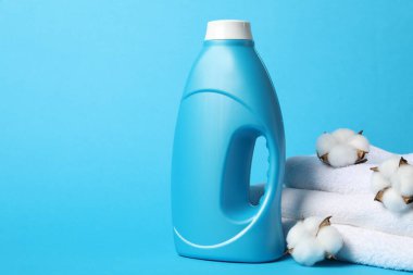 Bir şişe yumuşatıcı, pamuk çiçekleri ve açık mavi arka planda havlular, metin için alan