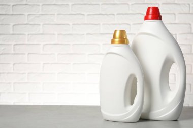 Beyaz tuğla duvara karşı gri masada yumuşatıcı şişeler, metin için yer