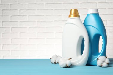 Beyaz tuğla duvara karşı açık mavi masada yumuşatıcı ve pamuk çiçekleri, metin için yer