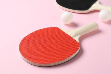 Pembe arka planda pinpon raketleri ve topları, yakın plan.