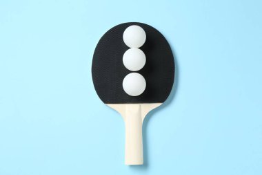 Masa tenisi raketi ve toplar açık mavi arkaplanda, üst görünümde.