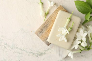 Bir kalıp sabun ve yasemin çiçekleri ışık masasında, düz yerde. Metin için boşluk