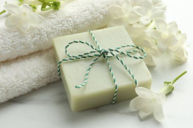 Bir kalıp sabun, yasemin çiçekleri ve beyaz mermer masaya havlu, yakın plan.