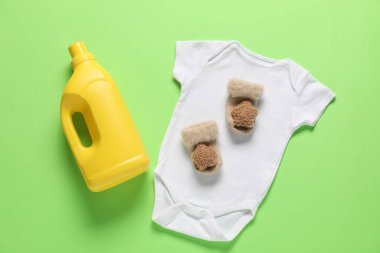 Bir şişe yumuşatıcı ve yeşil arka planda bebek kıyafetleri.