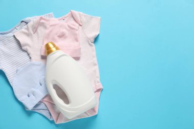 Bir şişe yumuşatıcı ve açık mavi arka planda bebek kıyafetleri. Metin için boşluk