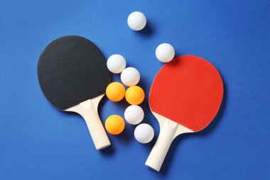 Masa tenisi raketleri ve topları mavi arka planda, düz yatıyordu.