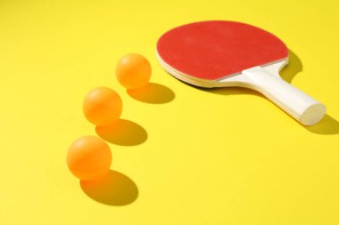 Sarı arka planda pinpon raketi ve toplar, yakın plan.