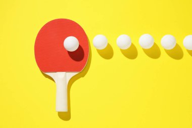 Masa tenisi raketi ve toplar sarı arka planda, düz yatıyordu