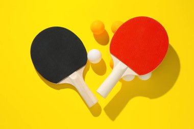 Masa tenisi raketleri ve topları sarı arka planda, düz yatıyordu.