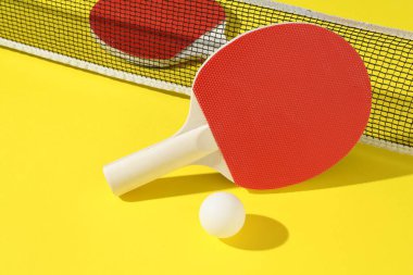 Ping pong raketleri, top ve ağ sarı arka planda, yakın plan