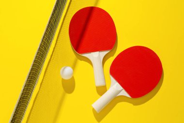 Ping pong raketleri, top ve ağ sarı arka planda, düz yatıyordu