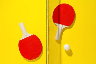 Ping pong raketleri, top ve ağ sarı arka planda, düz yatıyordu