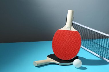 Masa tenisi raketleri, top ve ağ açık mavi masada. Metin için boşluk