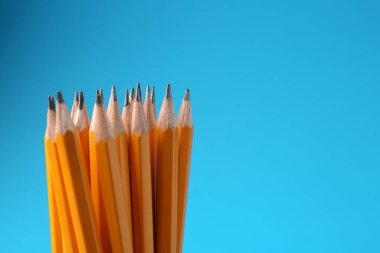 Açık mavi arka planda keskin grafit kalemler, yakın plan. Metin için boşluk