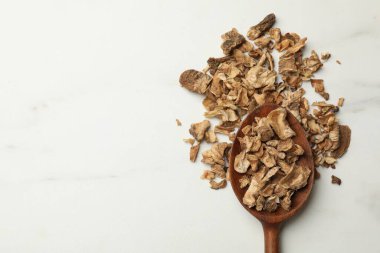 Beyaz masadaki kaşıkta kurutulmuş hindiba kökleri. Metin için boşluk