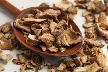 Beyaz masadaki kaşıkta kurumuş hindiba kökleri, yakın plan.