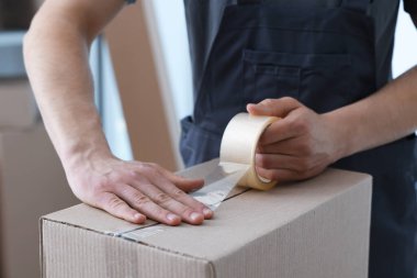 Kapalı alanda yapıştırıcı bantlı karton kutu mühürleyen adam.