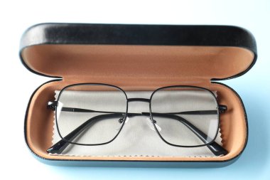 Açık mavi arka planda şık gözlüklü ve temiz kumaşlı çanta, üst görünümde.