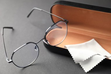 Gri arka planda şık gözlüklü ve temizlik bezli çanta, yakın plan.