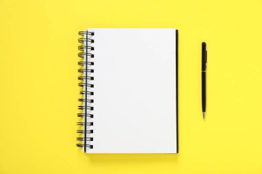 Sarı arka planda düz bir defter ve kalem var.