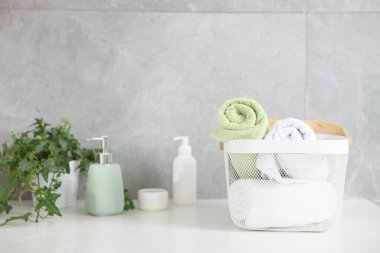 Sepetteki temiz havlular, kozmetik ürünler ve beyaz masa üzerindeki ev bitkisi.