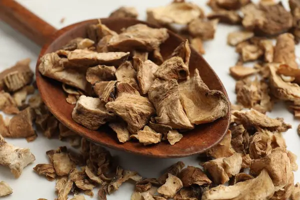 Beyaz masadaki kaşıkta kurumuş hindiba kökleri, yakın plan.
