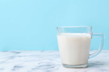 Açık mavi arka planda beyaz mermer masada bir fincan süt. Metin için boşluk