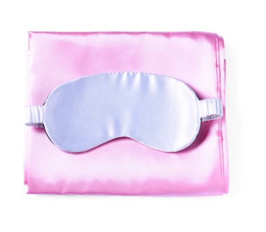 Beyaz arka planda ipek çarşaflar ve uyku maskesi, üst manzara.