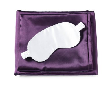 Beyaz arka planda ipek çarşaflar ve uyku maskesi, üst manzara.