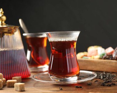 Geleneksel Türk çayı cam fincanlar, çaydanlık, kuru yapraklar, kahverengi şeker ve tatlılar ahşap masada, yakın plan