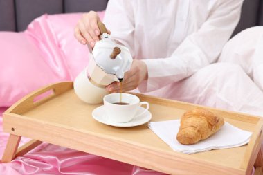 Kadın Moka çaydanlığından bardağa kahve dolduruyor pembe ipek çarşaflarla, yakın plan.