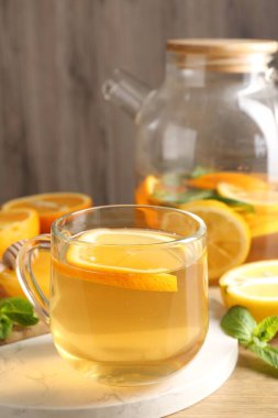 Cam fincanda aromatik meyve çayı, çaydanlık, portakal, limon, bal ve nane, ahşap masada, yakın plan.