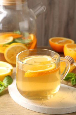 Cam fincanda aromatik meyve çayı, çaydanlık, portakal, limon, bal ve nane, ahşap masada, yakın plan.