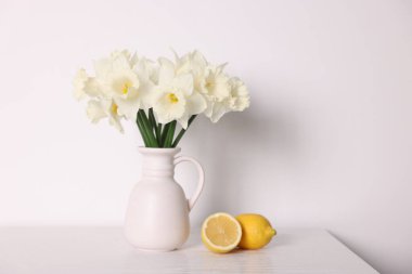 Vazodaki güzel nergisler ve beyaz ahşap masadaki limonlar