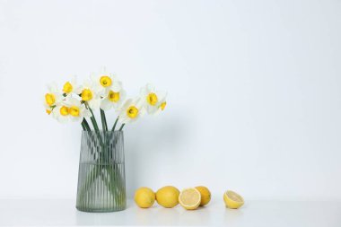 Vazodaki güzel nergisler ve beyaz masadaki limonlar.