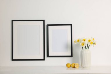 Beyaz masadaki vazodaki güzel nergisler ve kapalı alandaki resim çerçeveleri.