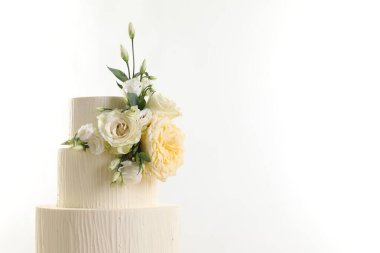 Beyaz arka planda çiçeklerle süslenmiş lezzetli düğün pastası, yakın plan. Metin için boşluk