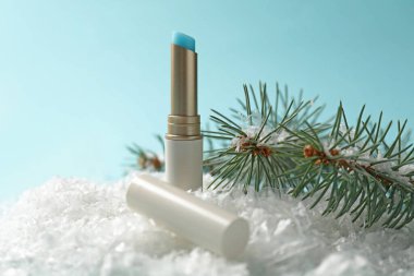 Nemlendirici dudak kremi ve yapay kar üzerindeki köknar ağacı dalları açık mavi arka planda, yakın plan. Kış bakımı