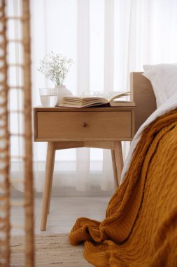 İçinde kitap olan komodin, vazoda çiçekler, yatağın yanında bir bardak su ve bardaklar.