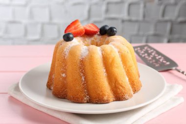 Pudra şekerli, dutlu ve pembe ahşap masadaki sunuculu lezzetli kek, yakın plan.